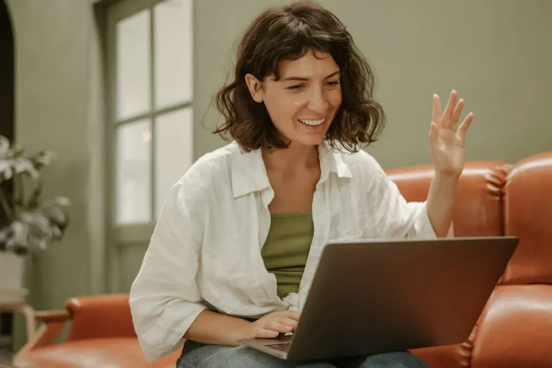 A woman smiling and waving at her laptop during a virtual meeting