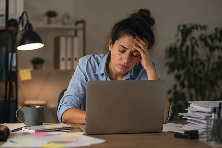 Young woman looking exhausted while working on a laptop in a home office